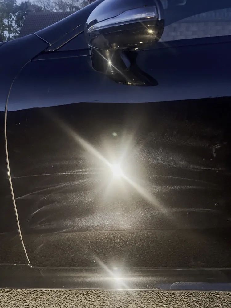 Black car door covered in swirl marks under a torch, before machine polishing